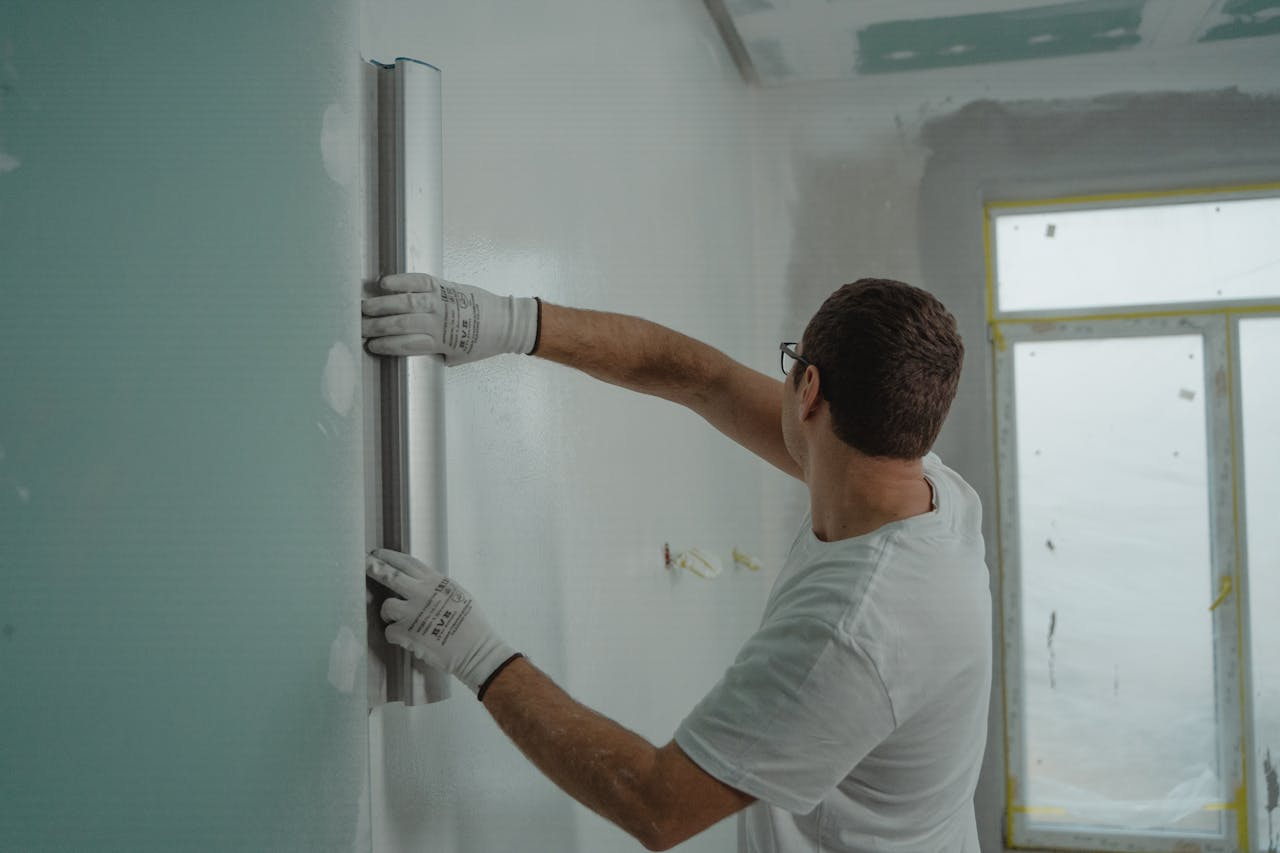 Services A man in a white shirt and gloves using a metal ruler for indoor wall renovation work.