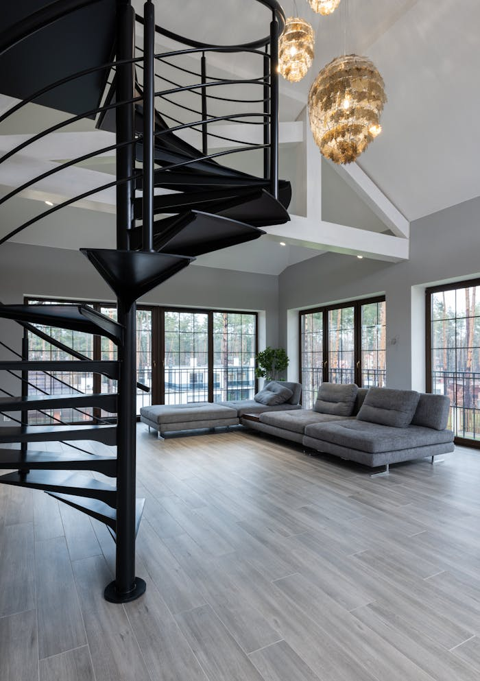 Interior of modern apartment with spiral stairway placed next to sofa and windows under chandelier